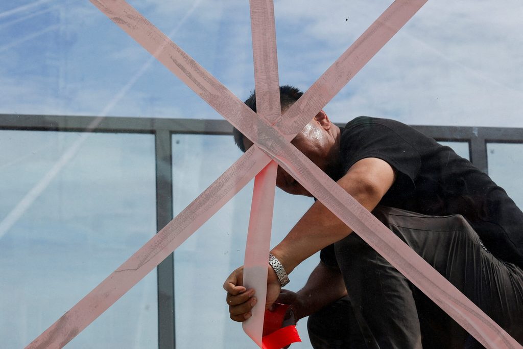 A person applies tape to a glass wall on a pedestrian bridge to secure it as Typhoon Bavi approaches Wenzhou