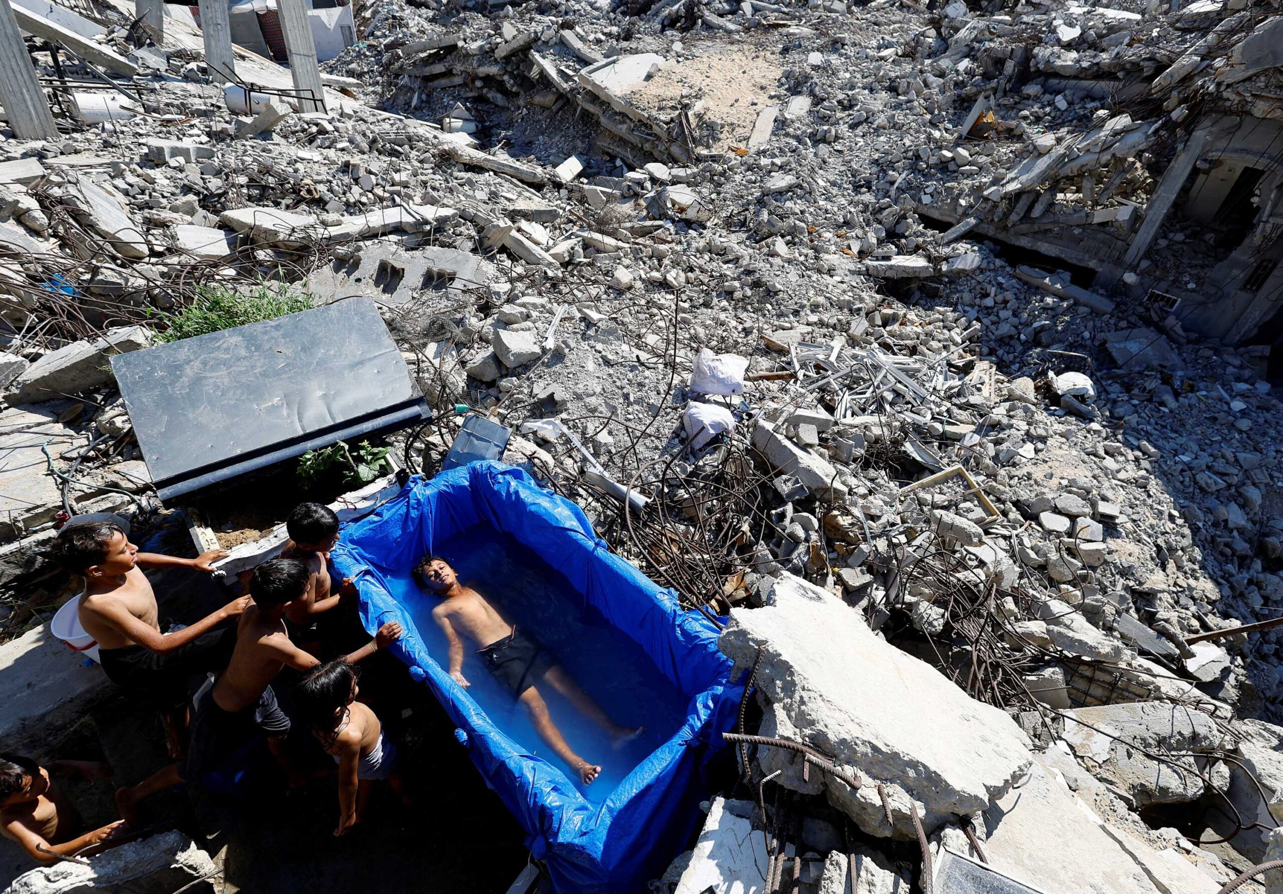 A Palestinian boy cools down in a makeshift pool on the remains of a house destroyed during the Israeli offensive, on a hot summer day in Beit Lahiya