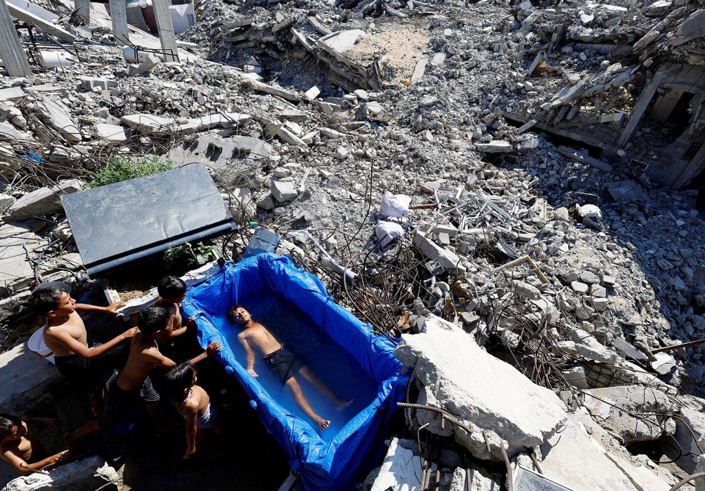 A Palestinian boy cools down in a makeshift pool on the remains of a house destroyed during the Israeli offensive, on a hot summer day in Beit Lahiya