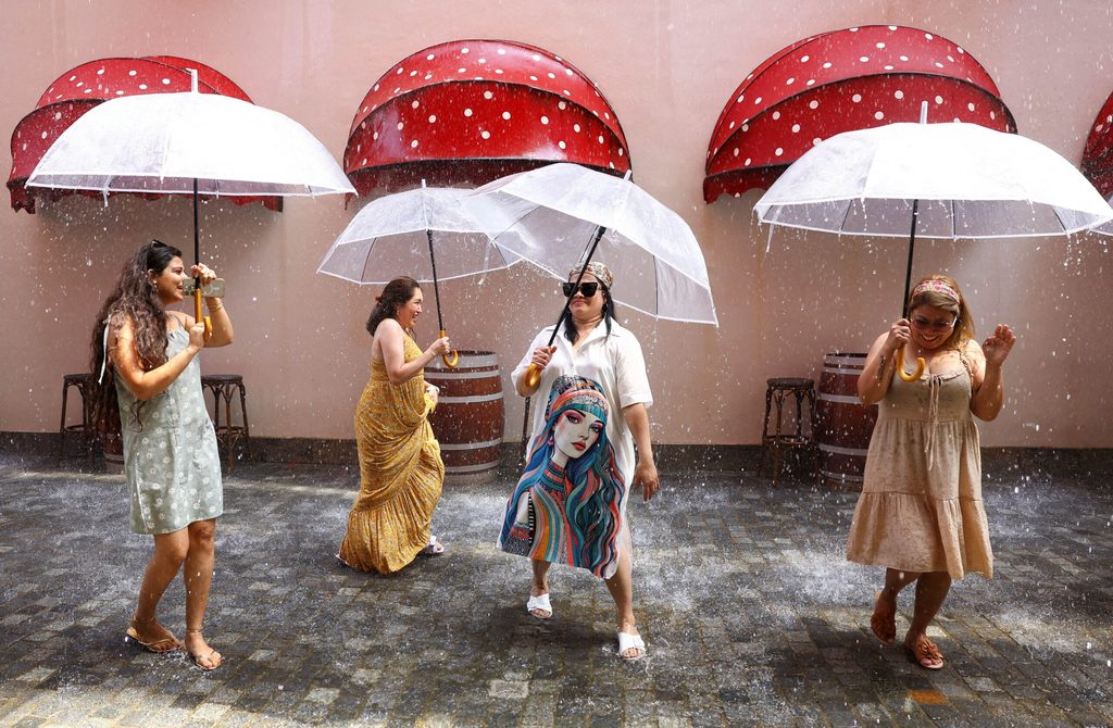 People dance with umbrellas on a climate-controlled “rainy street” at the voco Monaco Dubai resort on The Heart of Europe development in Dubai