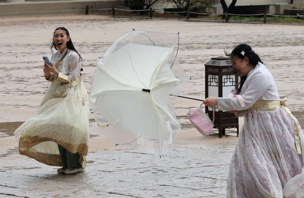 Tourists wearing Korean traditional costume Hanbok react as they make their way through strong winds at Gyeongbok palace in Seoul