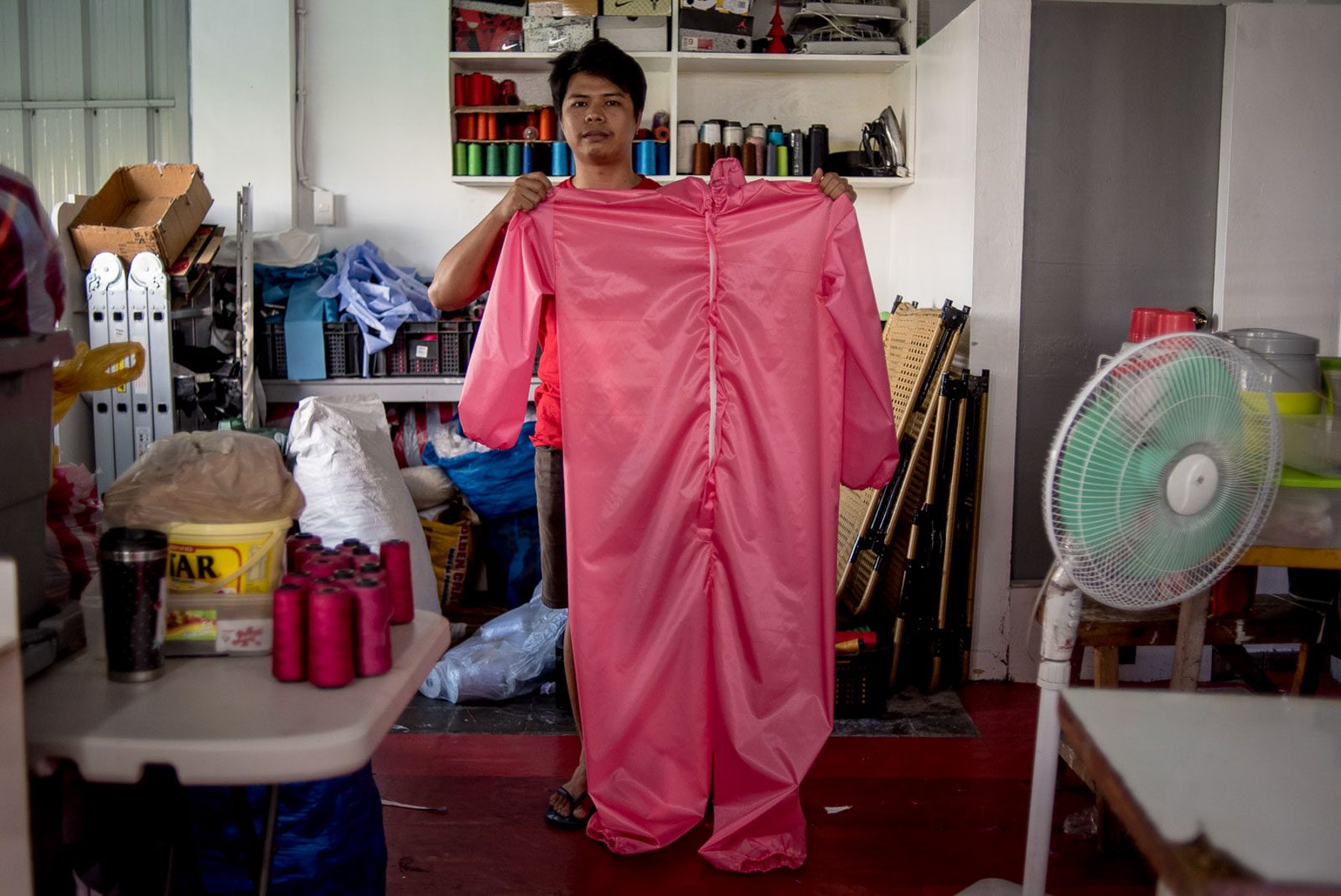 FINAL PRODUCT. A tailor holds a newly sewn PPE suit. 