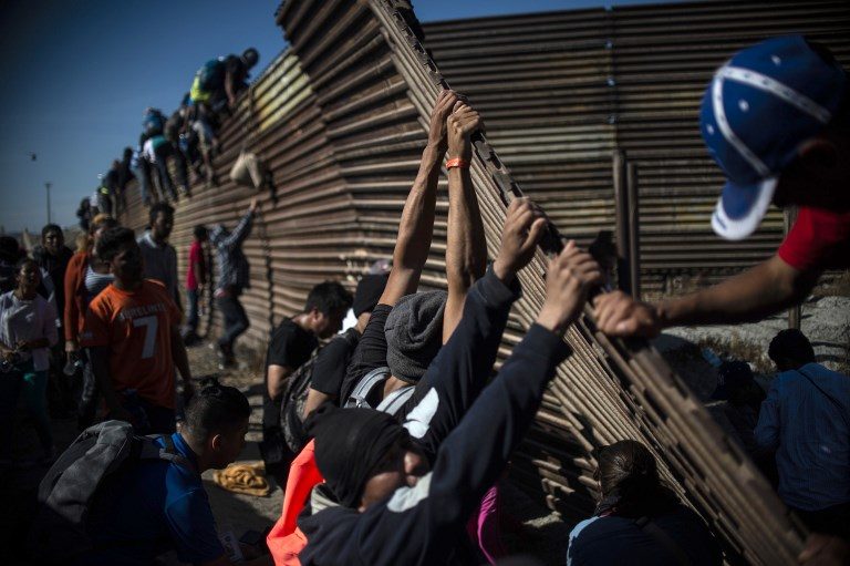 CROSSING BORDERS. Central American migrants climb the border fence between Mexico and the US as others try to bring it down, near El Chaparral border crossing, in Tijuana, Mexico, on November 25, 2018. Photo by Pedro Pardo/AFP   