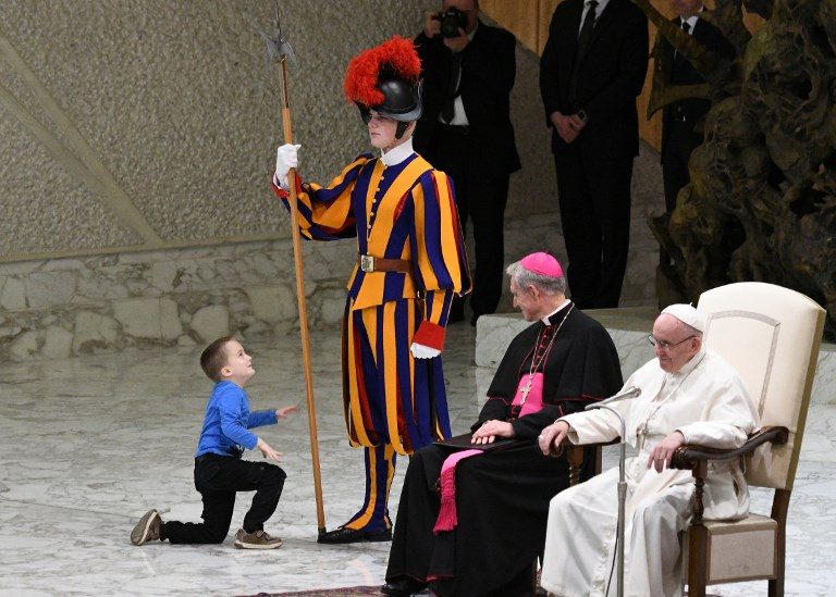 PAPAL AUDIENCE. Prefect of the Papal Household, Georg Ganswein (center) watches a boy who came from the audience onto the stage to play with the Swiss Guard's spear as Pope Francis (right) looks on during the weekly general audience on November 28, 2018, in Paul VI hall at the Vatican. Photo by Vincenzo Pinto/AFP   