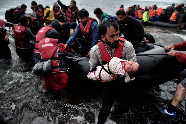 SAFE AND ASHORE. A migrant carrying his baby comes ashore along with other refugees and migrants arriving on the Greek Island of Lesbos on October 24, 2015 after crossing the Aegean sea from Turkey. Aris Messinis/AFP  