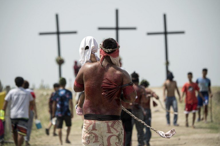 PENITENCE. A penitent carrying his daughter walks to the crosses during a reenactment of the crucifixion of Jesus Christ on Good Friday in Sitio Cutud, San Fernando, Pampang,a on March 30, 2018. Photo by Noel Celis/AFP    