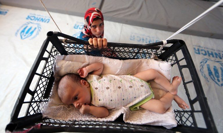 WAR CASUALTY. A displaced Iraqi girl swings her brother in a makeshift crib made from a fruit-basket as it hangs from the roof of a tent on June 5, 2017. Photo by Karim Sahib/AFP   