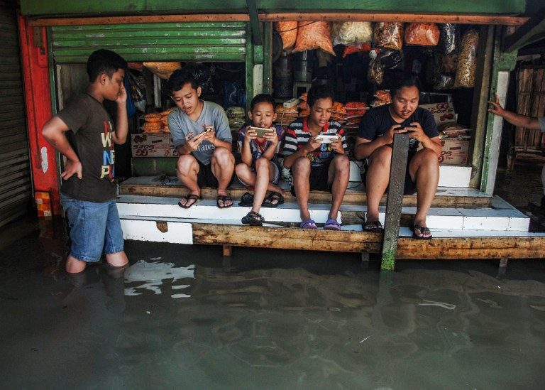 GAME ON. Indonesian youths sit on a table while playing games at a game center surrounded by floodwaters after seasonal rains hit the area around Bandung, West Java province, on November 17, 2017. Photo by Timur Matahari/AFP  