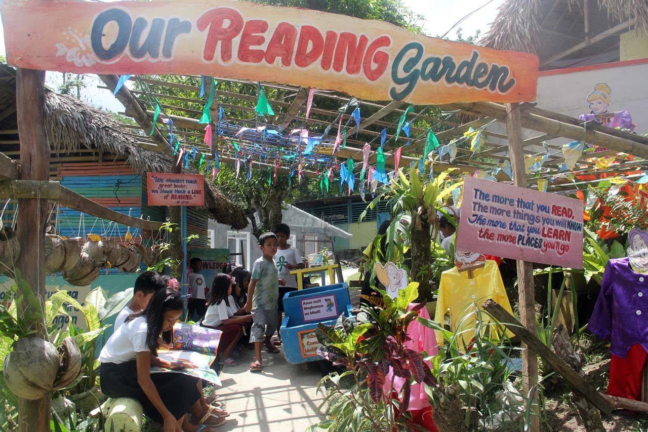 READING GARDEN. Children read outdoors in their Reading Garden, where a sign says, 'The more that you read, the more things you will know. The more that you learn, the more places you'll go.' 