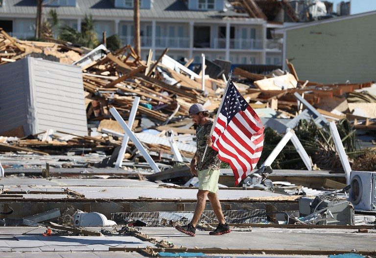 NOTHING LEFT. Kevin Guaranta carries an American flag he found as he walks on the foundations of what were homes that were demolished after Hurricane Michael passed through Mexico Beach, Florida, on October 12, 2018. Photo by Joe Raedle/Getty Images/AFP   
