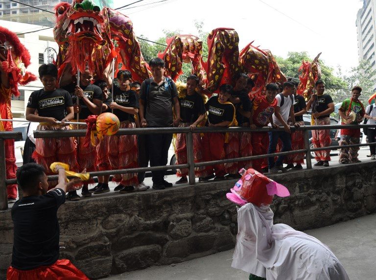 DRAGON DANCE. Children perform a lion dance routine with an improvised lion head made from a plastic pail, as members of a dragon dance troupe pass by, in the Chinatown district of Manila on February 4, 2019, on the eve of the Lunar New Year of the Pig. Photo by Ted Aljibe / AFP 