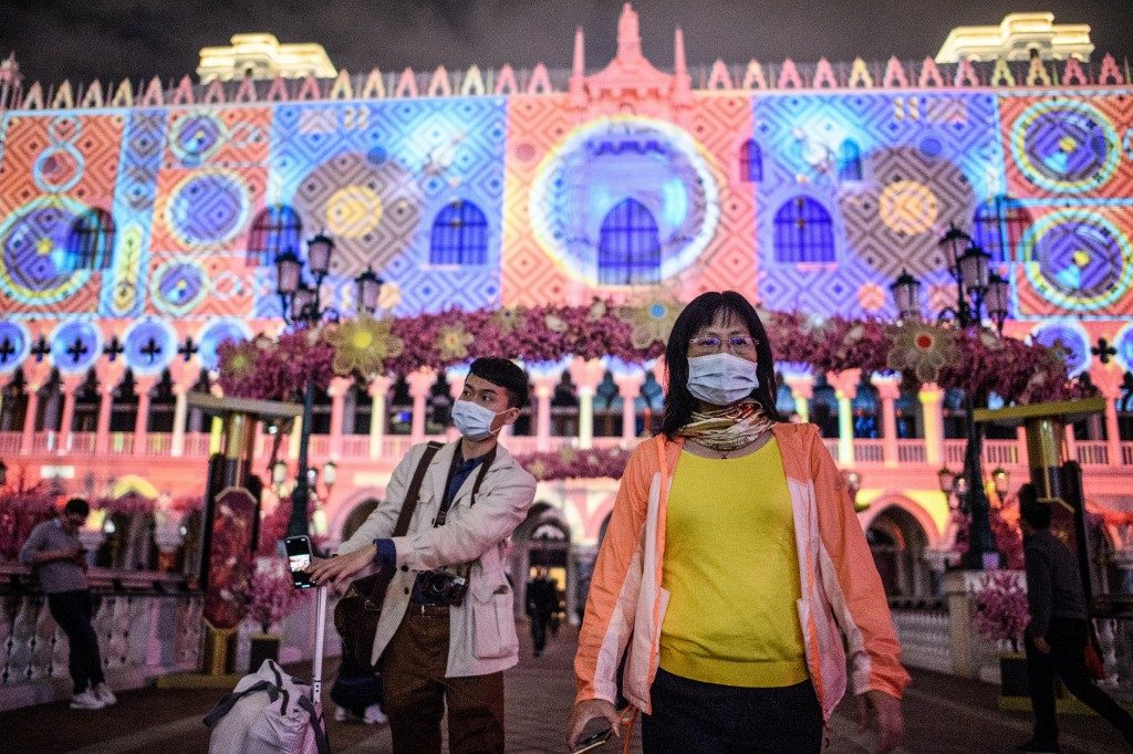 MACAU. Visitors wear face masks as they walk outside the Venetian casino hotel resort as a Lunar New Year light display is projected upon a facade of the building in Macau on January 22, 2020, after the former Portuguese colony reported its first case of the new SARS-like virus that originated from Wuhan in China. Photo by Anthony Wallace / AFP 