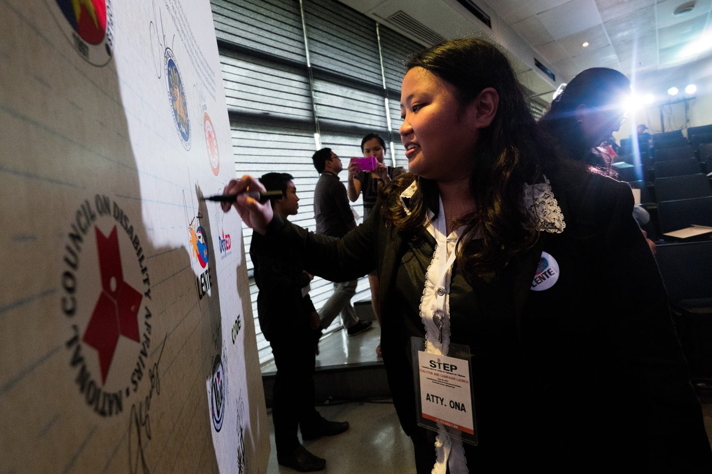 Attorney Rona Caritos, the acting executive director of LENTE, affixes her signature on a board that contains the logos of STEP Coalition's constituents. 
