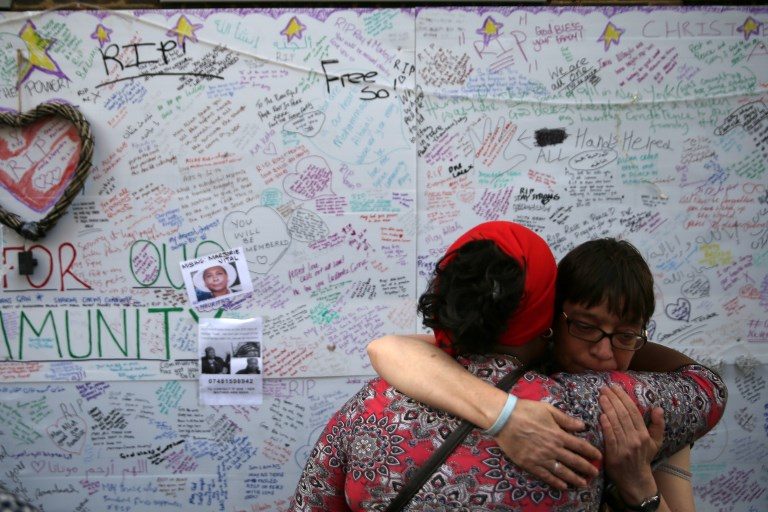 IN GRIEF. Two women embrace in front of messages left on a wall of condolence following the blaze at Grenfell Tower in west London on June 15, 2017. Photo by Daniel Leal Olivas/AFP   