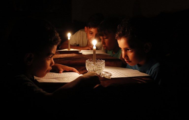 POWER SHORTAGE. Palestinian children at home reading books by candlelight due to an electricity shortage in Gaza City on June 13, 2017. Photo by Thomas Coex/AFP   