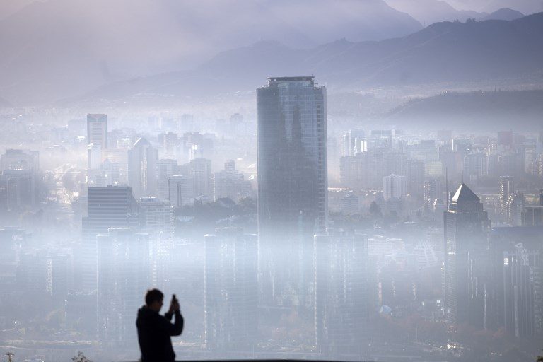 POLLUTED AIR. A person takes a picture of the smog over Santiago on July 9, 2018, as Chilean authorities declared a new environmental pre-emergency due to high levels of air pollution. Photo by Claudio Reyes/AFP PHOTO   