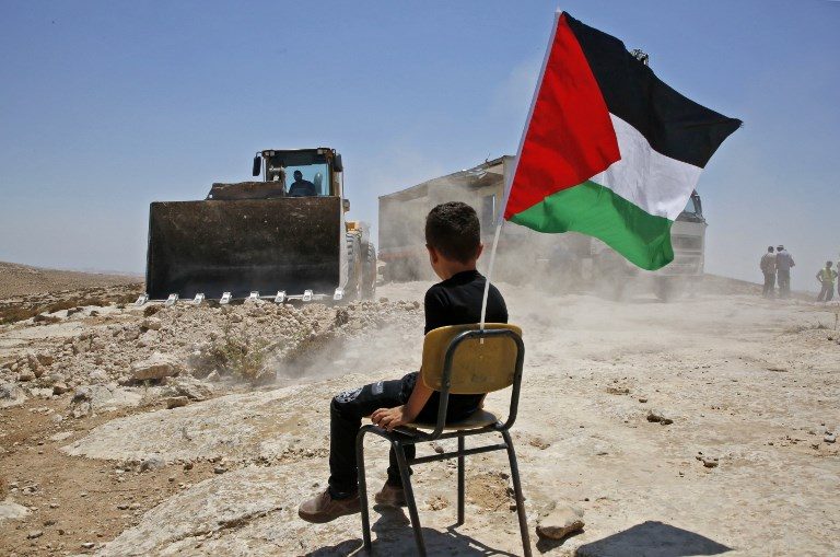 GONE. A Palestinian boy sits on a chair with a national flag as Israeli authorities demolish a school site in the village of Yatta, south of the West Bank city of Hebron, and to be relocated in another area, on July 11, 2018. Photo by Hazem Bader/AFP   