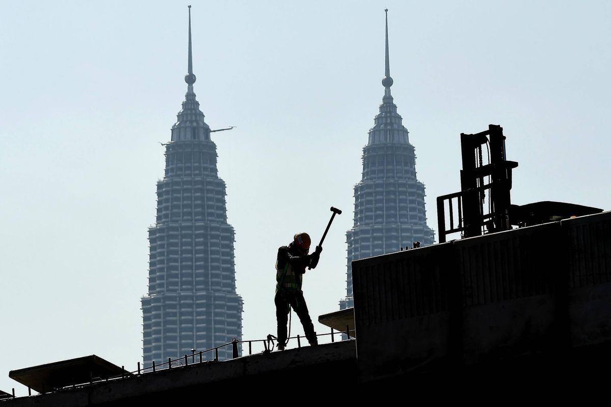 PEKERJA. Seorang pekerja tengah bekerja di depan Menara Petronas di Kuala Lumpur. Foto oleh AFP 