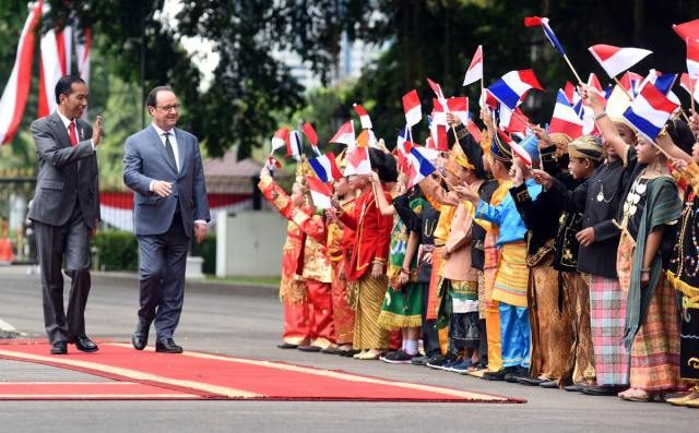 SAMBUT ANAK-ANAK. Presiden Republik Perancis, Francois Hollande (kanan) tersenyum ketika disambut anak-anak yang membawa bendera Indonesia-Perancis di halaman Istana Merdeka. Foto diambil dari akun @setkabgoid 