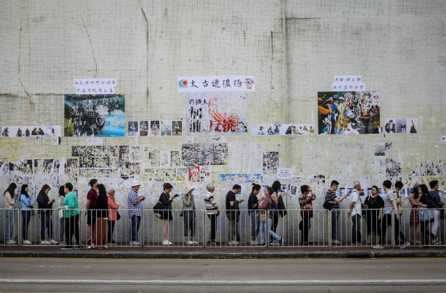 VOTE. People queue to cast their vote in front of a 'Lennon Wall' adorned with tattered posters in support of the ongoing protests, during the district council elections in Tai Koo in Hong Kong on November 24, 2019. Photo by Vivek Prakash/AFP 