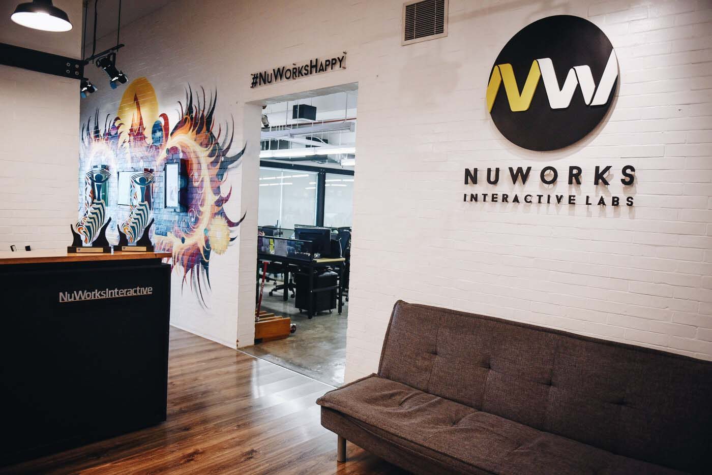 A portion of the lobby where touch screen television screens display the company's best works. By the entrance of the workspace, employees are reminded of the company's #NuWorksHappy philosophy.
