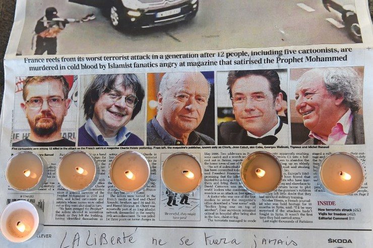 Candles are placed on a newspaper bearing pictures from (L) of French satirical weekly Charlie Hebdo's editor and cartoonists Charb, Jean Cabut, aka Cabu, Georges Wolinski and Michel Renaud who were killed the day before in an attack by two armed gunmen on the offices of French satirical newspaper Charlie Hebdo, during a gathering in Marseille, on January 8, 2015. Anne-Christine Poujoulat/AFP