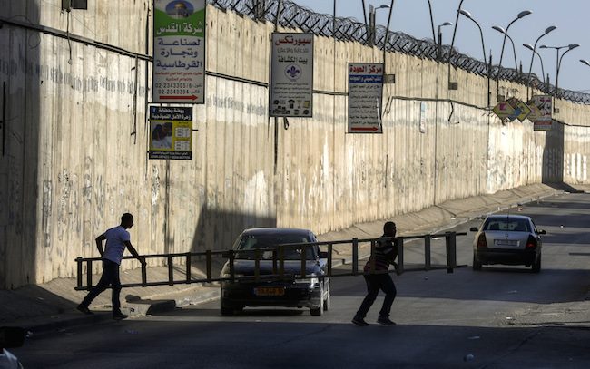 Warga Palestina yang dilarang melintas ke Jerusalem menggunakan tangga untuk melintasi dinding pembatas di kota Al Ram, di utara Jerusalem. Mereka membawa tangga sendiri demi salat di masjid Al Aqsa. Foto: EPA/ATEF SAFADI 