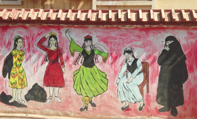 PROPAGANDA MURAL. A propaganda mural in Turpan, Xinjiang, 2017, encouraging women to cast off their Islamic dress and embrace their so-called indigenous culture. 
Â© Coda Story 