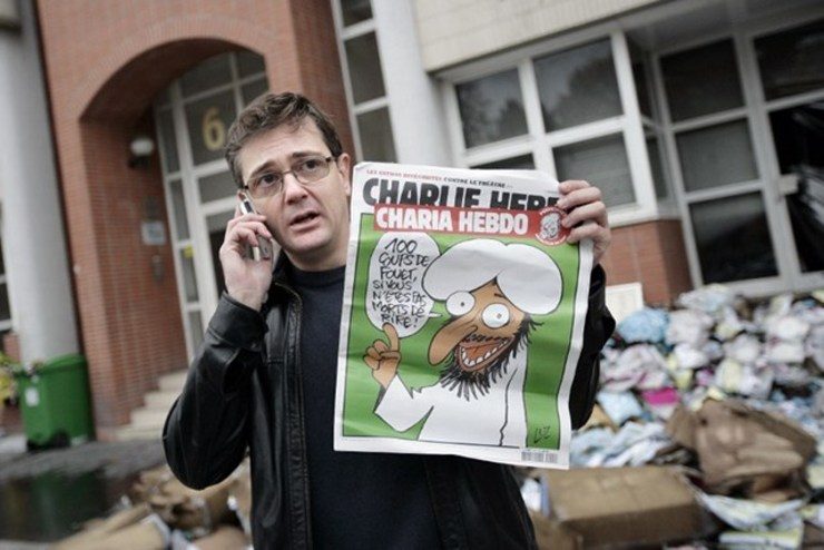 CONTROVERSIAL PHOTO. Some news organizations decided to blur the magazine cover in this photo. Charlie Hebdo's slain publisher known as Charb, uses his cell phone as he shows a special edition of French satirical magazine on November 2, 2011 in Paris. The cover features a cartoon of a grinning, bearded figure, saying: ‘100 lashes if you don't die of laughter!’ File photo by Alexander Klein/AFP 
