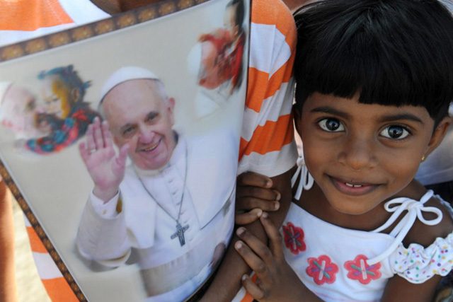 A young Sri Lankan holds paraphernalia bearing the portrait of Pope Francis as she waits for his arrival in Colombo on January 13, 2015. Photo by Lukruwan Wanniarachchi/AFP