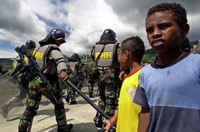 Warga Papua menyaksikan aparat Kepolisian bersiap mengantisipasi kerusuhan di foto ini yang diambil pada tahun 2000. Foto oleh AFP 