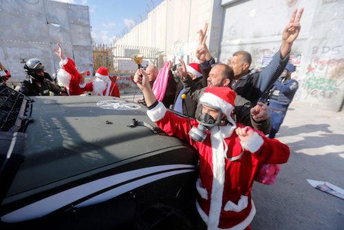 Seorang warga Palestina berkostum Santa Claus dan berdemo di depan tembok yang memisahkan negara itu dengan Israel dalam aksi anti-Israel di West Bank, Bethlehem, 18 Desember 2015. Foto oleh Abed Al Hashlamoun/EPA  