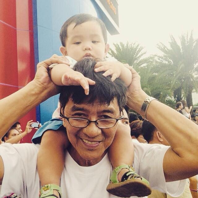 A grandfather carries his grandson who is barely a year old, while waiting for Pope Francis in MOA