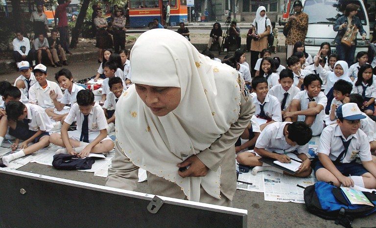 CONFUSING CURRICULUM. A primary school teacher (C) writes on a class board as children sit on the pavement attending a class outdoors in Jakarta. File photo by AFP