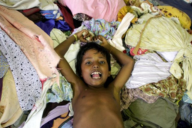CLOTHES, FINALLY. A Rohingya child lies among the used clothes donated by the local people at Lhok Sukon stadium, North Aceh, Indonesia, 12 May 2015. More women and children take the risk to go out to sea to find better life outside of Myanmar. File photo by Zikri Maulana/EPA 