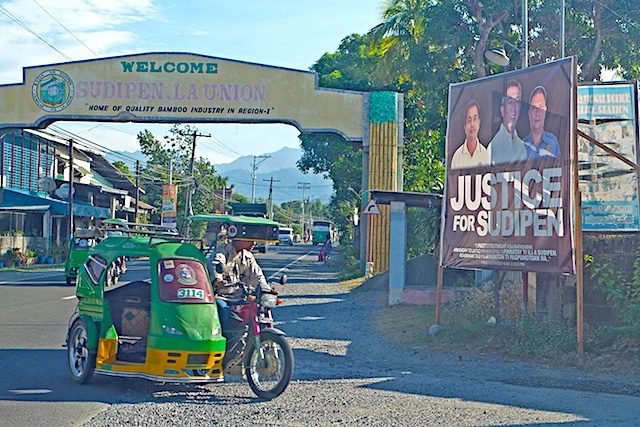 SUPIDEN. A poster with the image of the late mayor Alexander Buquing flanked by his driver and bodyguard, all killed in an ambush in October 1, stands near the welcome arch of Supiden town 