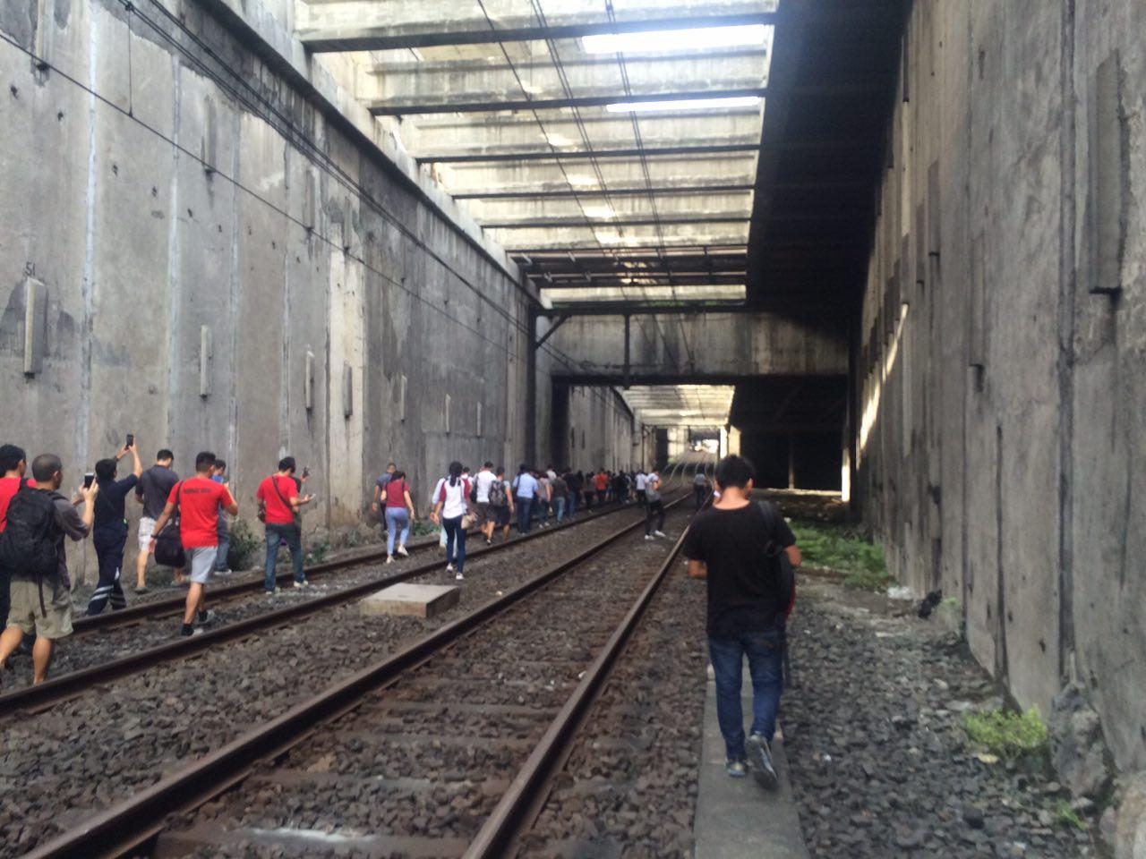 Commuters walk along MRT3 tracks as coach gets detached from train