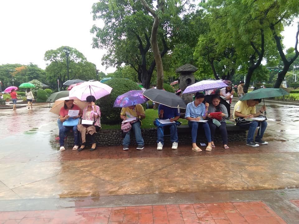 BRAVING THE RAINS. People try to keep themselves dry as they fill out job applications at the government job fair Luneta on a rainy June 12, 2018. Photo from DOLE 