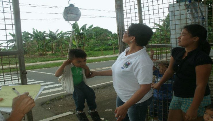 HOUSEHOLD. A BNS weights a child to check if he's underweight. Photo from the Barangay Nutrition Scholars Federation