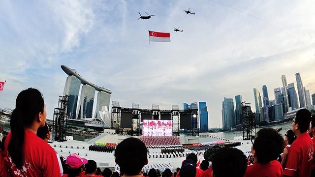 POMP AND CIRCUMSTANCE. Singaporeans watch helicopters holding up the national flag on Singapore National Day. 