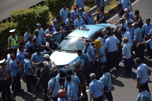 Puluhan sopir taksi melakukan aksi sweeping terhadap satu armada Blue Bird, saat melakukan demonstrasi pada Selasa, 22 Maret untuk menuntut penutupan transportasi berbasis aplikasi. 
