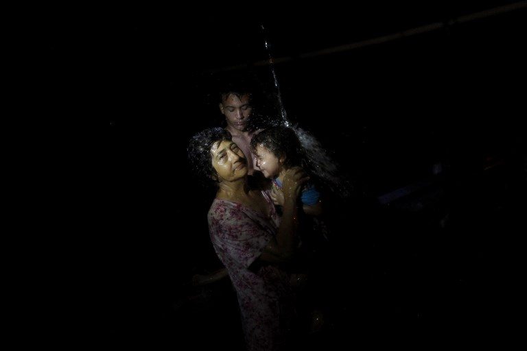 IN THE DARK. A woman affected by Hurricane bathes a child using an improvised water system for water pipes from a mountain creek in Utuado, Puerto Rico, on October 17, 2017. Photo by Ricardo Arduengo/AFP  