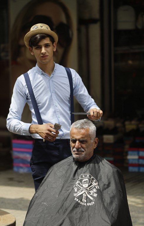 THE TALL ONE. Mohammed, a Lebanese roaming barber better known as 'Abo Tawila,' (the tall one in Arabic) gives a client a haircut on a sidewalk in the Lebanese capital Beirut's southern suburbs. Photo by Joseph Eid/AFP 