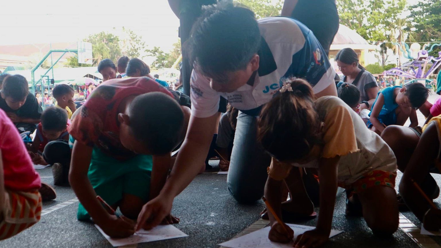 MORE THAN GIFTS. A volunteer in Lingayen, Pangasinan assists kids in writing during an outreach event at the plaza. Photo courtesy of Jerico Samson  