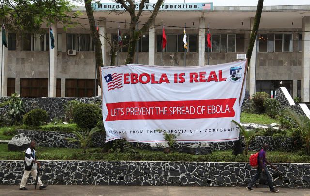 EBOLA IS REAL. Liberian men walk past an Ebola banner at the Monrovia City Hall in Liberia, 31 July 2014. Ahmed Jallanzo/EPA