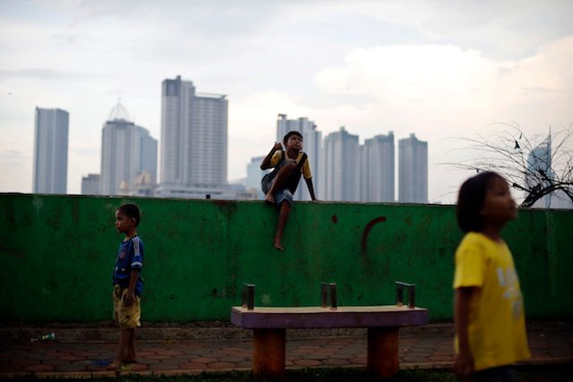 Anak-anak bermain di sebuah daerah kumuh dengan latar belakang bangunan gedung tinggi di Jakarta. Foto oleh EPA 