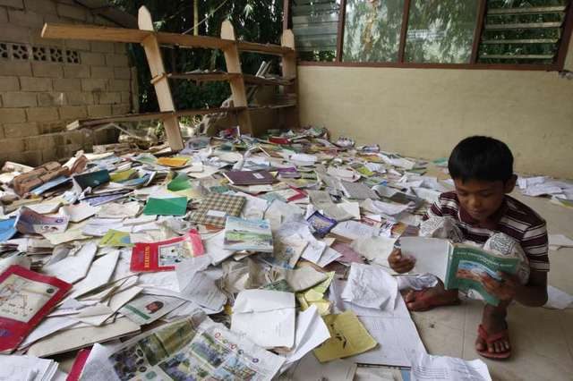Seorang anak di Padang Sumatera Barat sedang membaca buku di perpustakaan yang rusak akibat gempa bumi. Foto oleh MAST IRHAM/EPA 