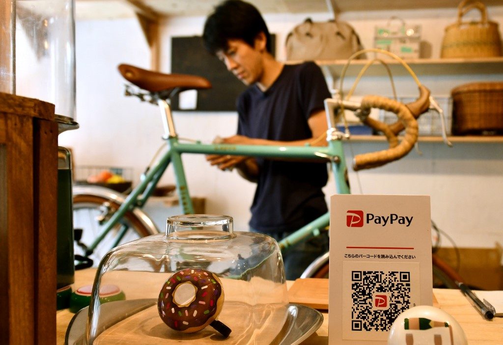 This photo taken on July 25, 2019 shows bike repair shop owner Katsuyuki Hasegawa working on a bicycle at his shop in Tokyo, next to a notice offering customers the option to settle their bill via PayPay -- a tie-up between Softbank and Yahoo. Photo by Toshifumi Kitamura/AFP 