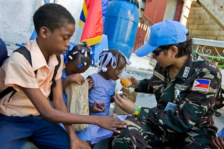 A member of the Filipino contingent of the United Nations Stabilization Mission in Haiti (MINUSTAH) helps a young student of the Baptist Theological and Orphanage School drink juice. 24 October 2008, Port au Prince, Haiti. Mark Dormino/UN Photo