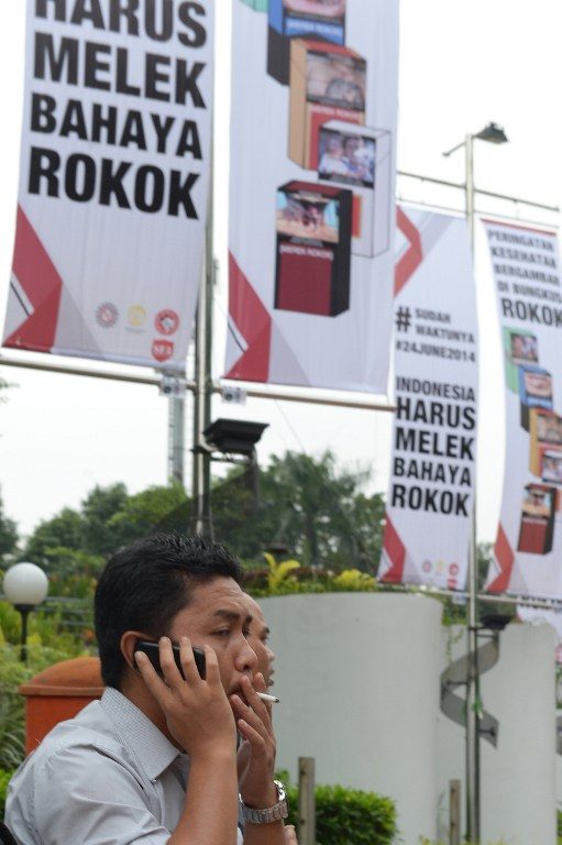 TIDAK PEDULI. Seorang perokok merokok di bawah papan reklame berisi kampanye anti-rokok. Foto oleh Adek Berry/AFP  